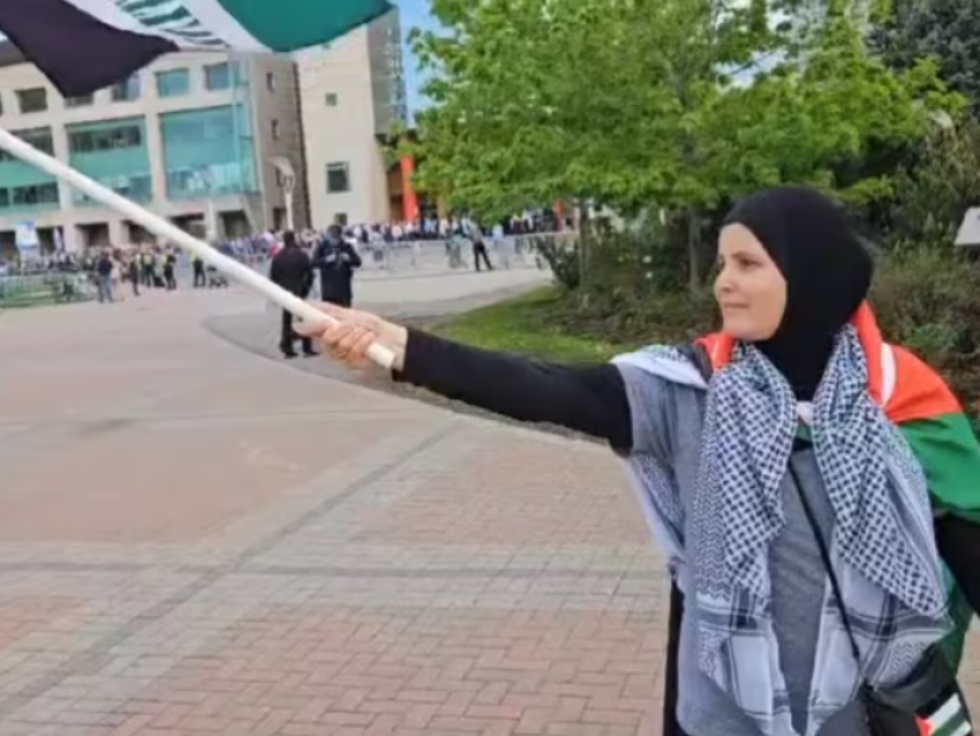 A screenshot of a video showing Hayfa Abdelkhaleq waving a Palestinian flag outside Ottawa City Hall during a flag-raising ceremony in honour of Israel&#039;s Independence Day. Moments later, a woman pulled down her hijab.