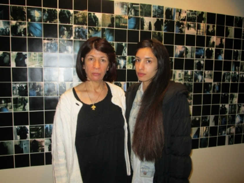 Rehab Nazzal with her daughter Rana Nazzal in front of photos of a raid on Palestinian prisoners. Smiling didn&#039;t seem appropriate given the context.