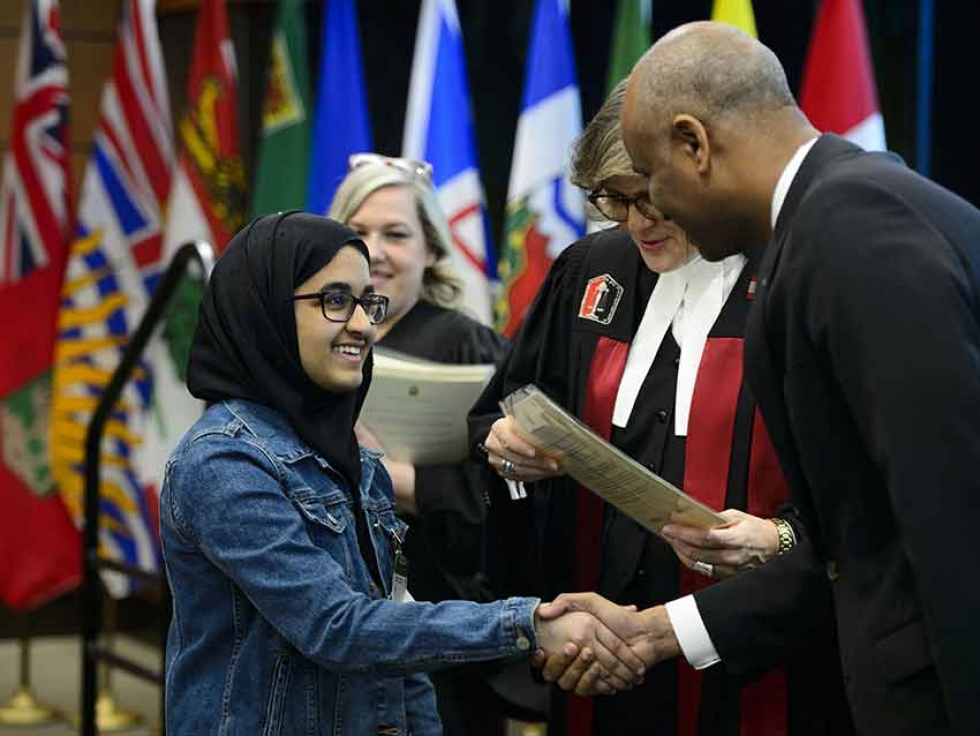 A youth receives her Certificate of Citizenship from Immigration Minister Ahmed Hussen and Citizenship Judge Marie Senecal-Tremblay on Parliament Hill in Ottawa on April 17, 2019