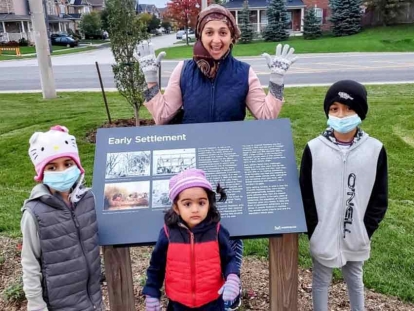 Zaineb Survery with her three children in front of one of the signs documenting the history of Churchill Meadows.