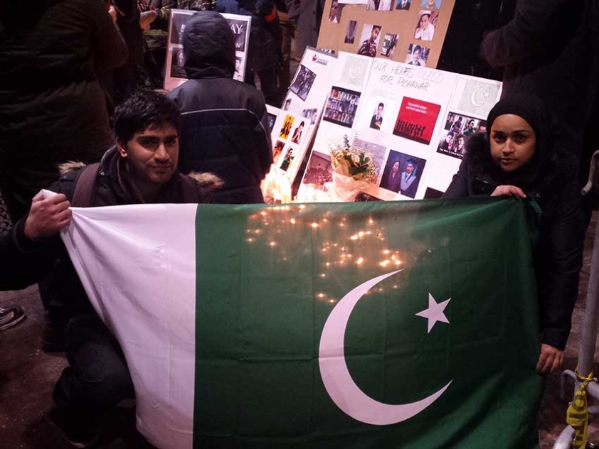 At the vigil held in front of City Hall, university students Samer Abed and Sonia Hamid hold a Pakistani Flag in front of the pictures of those killed in the Peshawar School Attack.