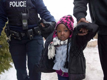  This 2017 photo shows a young asylum seeker being held by an RCMP officer and her father after crossing the border into Canada from the United States. THE CANADIAN PRESS/Paul Chiasson
